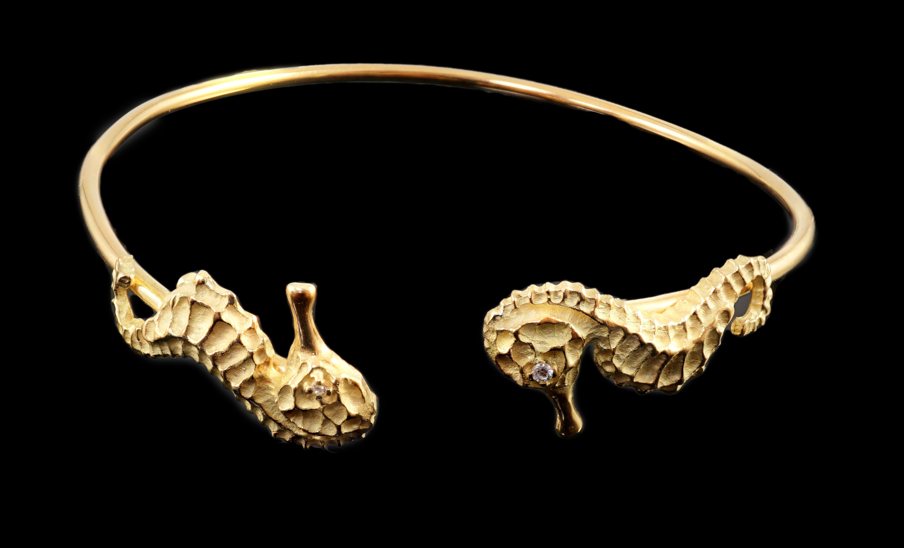 A modern gold and diamond chip set open work bangle, each terminal modelled as a seahorse with diamond chip eye